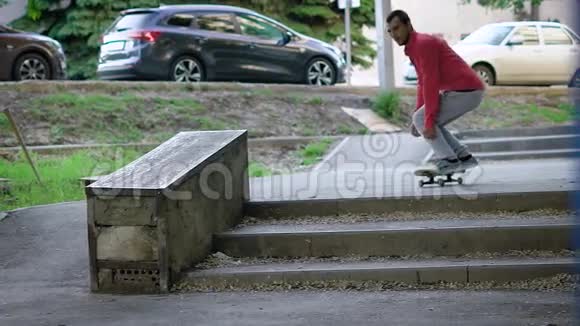 一个热爱自己年轻爱好的成人滑板运动员跳在楼梯的路边以便在楼梯上表演滑滑梯视频的预览图