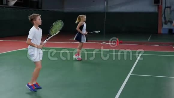 女孩和男孩在室内球场打网球年轻球员练习视频的预览图