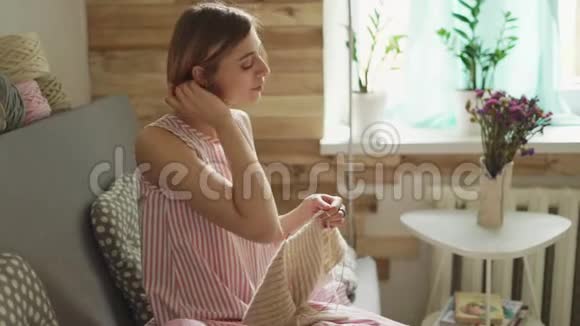 女工匠在背景窗的房间里坐在沙发上编织羊毛视频的预览图