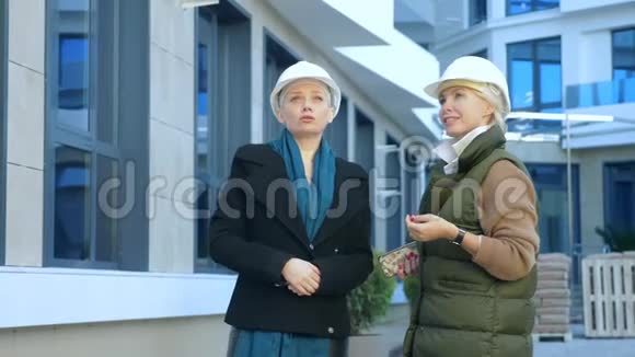 两个戴白盔的妇女在大楼的背景上交谈视频的预览图