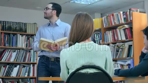 有书的年轻男教师与图书馆的学生交谈视频的预览图