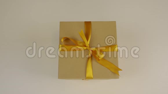 白种人的手从白色的桌子上拿走棕色的礼盒带蝴蝶结的金色丝带一个礼品盒概念庆祝活动视频的预览图