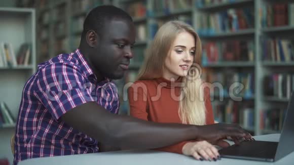 欧洲女士和非裔美国人花时间在图书馆的笔记本电脑上视频的预览图