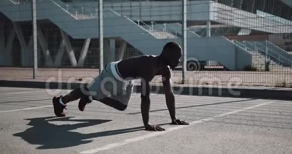 美国黑人运动员在体育场附近的街道上快速地在前面的木板上弯曲双腿健身健康视频的预览图