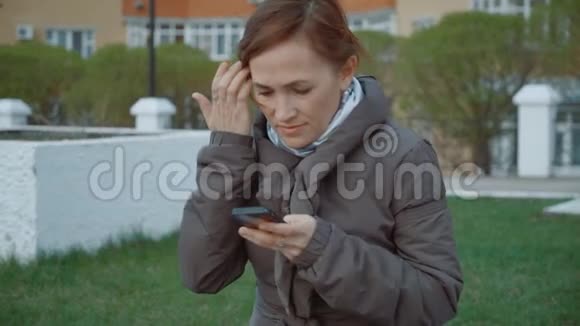 一个穿着棕色夹克的漂亮女人在长凳上收到了一条手机短信视频的预览图