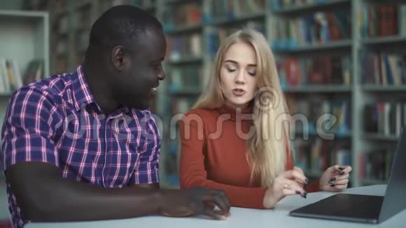 欧洲女士和非裔美国人带笔记本电脑在图书馆学习视频的预览图