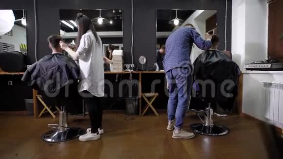理发师和他的同事给两个来美容院为男士理发的男人理发顾客坐在扶手椅上视频的预览图