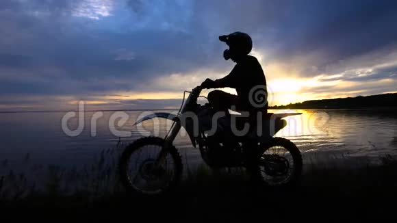 莫托科罗斯骑手在他的Enduro自行车启动引擎日落天空和河流视频的预览图