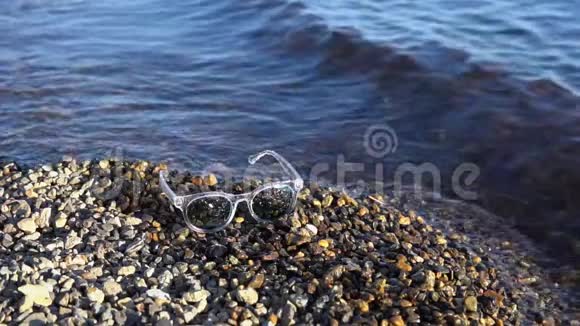 太阳镜躺在鹅卵石海滩上海浪在岸边飞溅视频的预览图