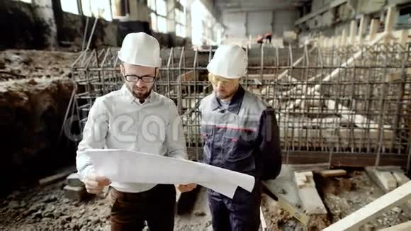 两个人在为蓝图工作承包商和现场工人调查蓝图并在背景下团队工作视频的预览图