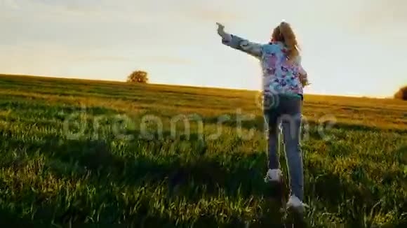 一个小女孩像飞机一样跑过田野日落时分概念青春的能量快乐的童年梦想视频的预览图