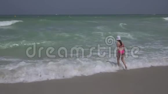 穿着泳衣的少女在迪拜海滩上快乐地跳进波斯湾的海浪中视频的预览图
