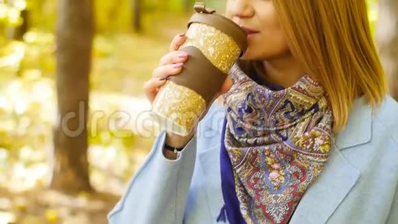 可爱的年轻女子在秋天的公园里喝杯咖啡视频的预览图