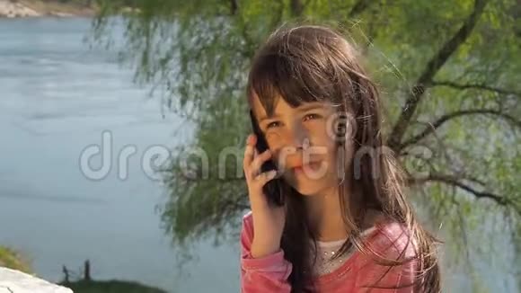 在水边拿电话的小女孩这孩子在露天一个女孩在阳光明媚的春天在河边视频的预览图