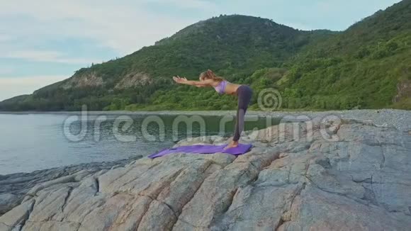 苗条的女孩弯曲瑜伽姿势在岩石上对抗海洋视频的预览图