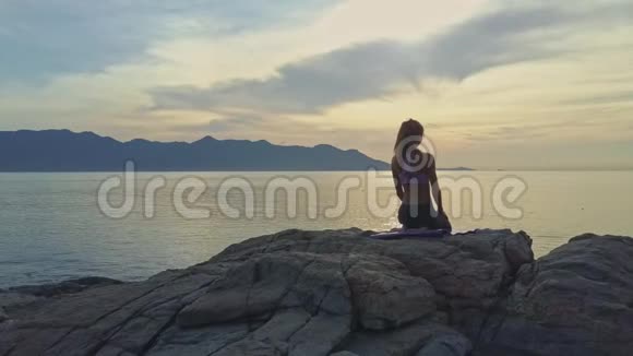 在金色日出海洋中坐着瑜伽姿势的无人观瞻女孩视频的预览图