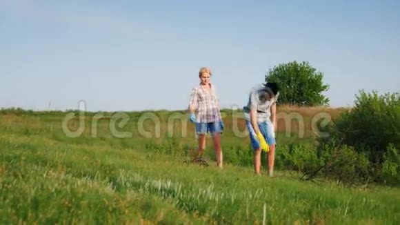 两名志愿者一男一女在靠近森林的草地上清理垃圾和干树枝视频的预览图