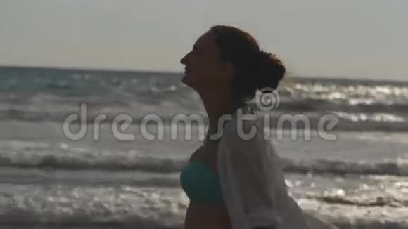 快乐的女人穿着比基尼和衬衫在海边散步举起手年轻漂亮的女孩享受生活视频的预览图
