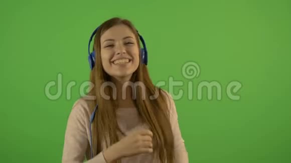 一个漂亮的年轻白人模特通过耳机和舞蹈听音乐在绿色的背景上视频的预览图