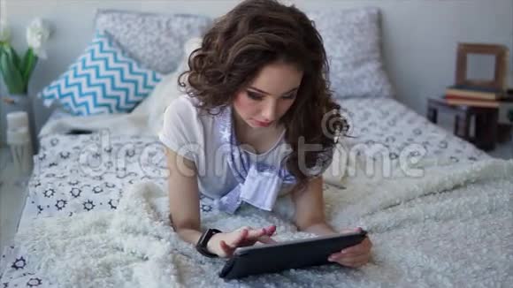 年轻女子一边笑一边看着卧室里的平板电脑屏幕视频的预览图