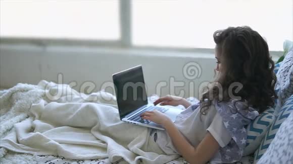 成年女孩在笔记本电脑键盘上打印文本躺在床上的毯子下面视频的预览图