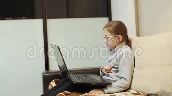 戴眼镜的女孩坐在沙发上笔记本电脑上看起来很卡通视频的预览图