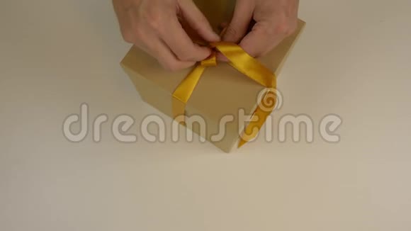 关闭顶部视图高角度曼斯手在棕色纸箱礼盒上用缎带做蝴蝶结白色米色背景视频的预览图