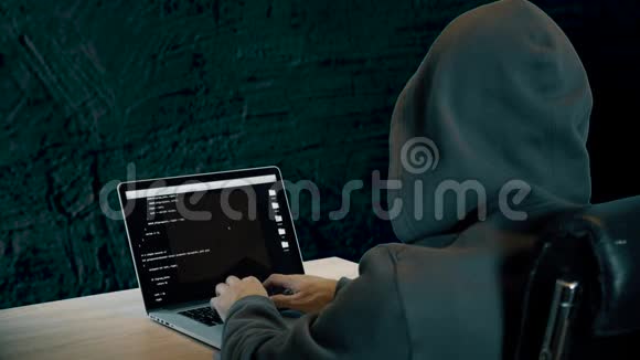 哈克坐在有混凝土墙的房间里的桌子旁在笔记本电脑键盘上打字的人破解密码视频的预览图
