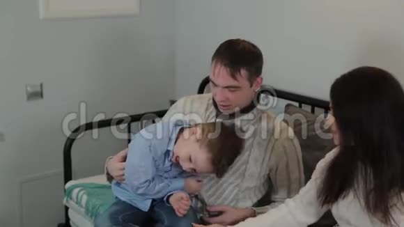 美丽而快乐的爸爸妈妈和儿子在沙发上的现代内部视频的预览图