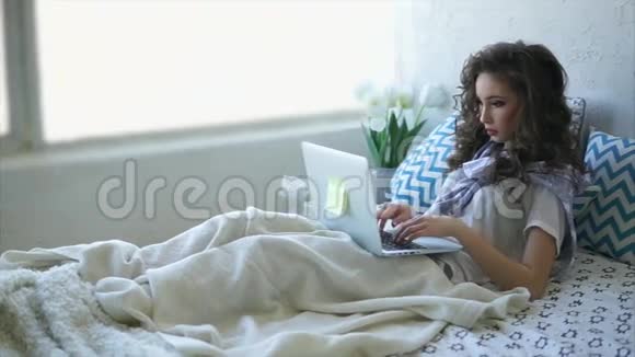 年轻女子躺在卧室的床上在网上和朋友聊天视频的预览图