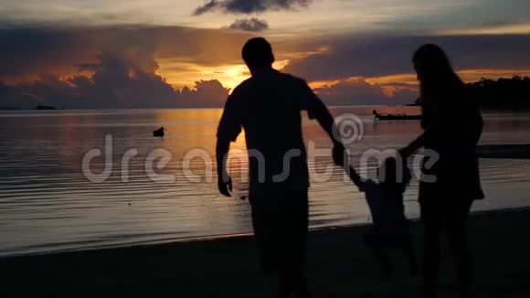 日落时一家人带着一个孩子在海滩上散步和玩耍剪影式视频的预览图