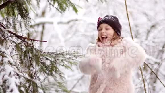 冬天森林里的一个美丽的女孩在雪地里快乐她穿着一件粉红色的外套手套和一顶黑色的帽子视频的预览图