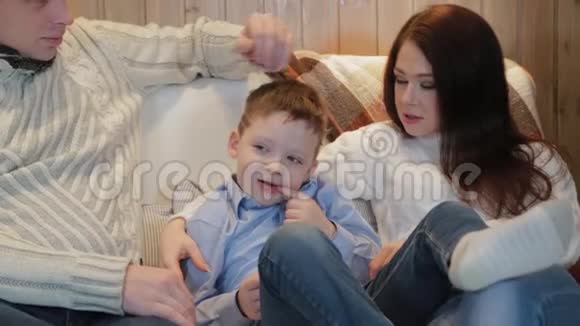 美丽而快乐的爸爸妈妈和儿子在沙发上的现代内部视频的预览图