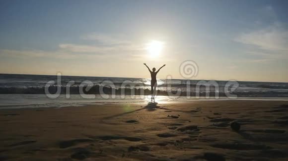 日落时分年轻女子在海边散步举起双手美丽的少女站在海边视频的预览图