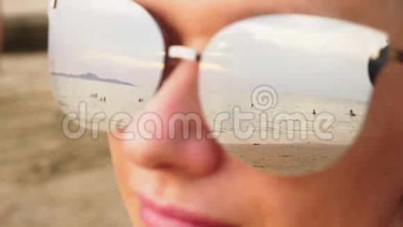 一个戴太阳镜的快乐女人的特写脸与休息的人的海滩反映在眼镜上视频的预览图