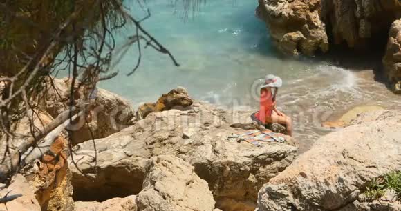 年轻漂亮的女人穿着泳衣躲在海边的岩石上视频的预览图