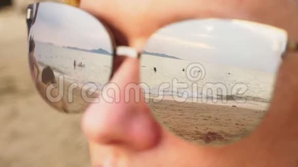 一个戴太阳镜的快乐女人的特写脸与休息的人的海滩反映在眼镜上视频的预览图