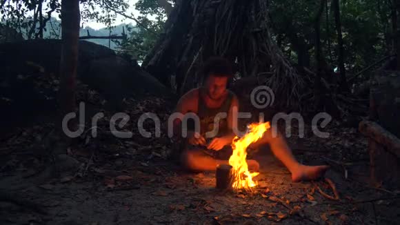 白种人野蛮人在热带森林里燃烧小篝火在暮色中煮水壶和米饭作为晚餐视频的预览图