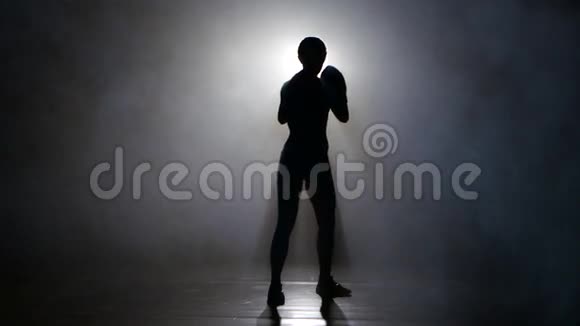 冠军拳击手在烟雾中发出踢剪影后方有灯光黑色背景视频的预览图