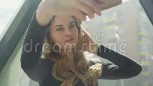 自拍照片靠窗美丽的女孩微笑手机与触摸屏使一个年轻的女人一个照片视频的预览图