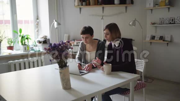 两个有创造力的女人在桌上用笔记本上网购物视频的预览图