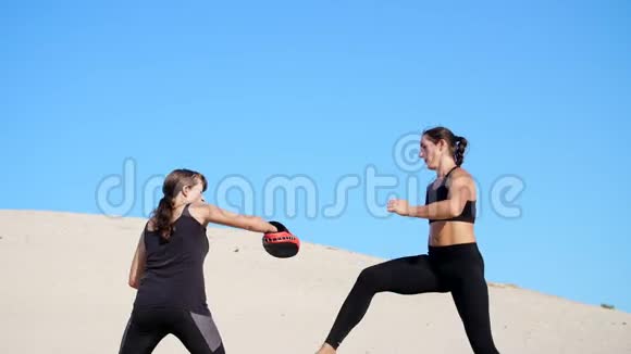 两个穿着黑色健身服的年轻女子在荒无人烟的海滩上做一对踢腿训练比赛视频的预览图