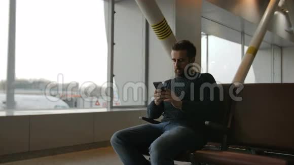 城市胡须男用智能手机在机场内旅行帅哥男模特视频的预览图