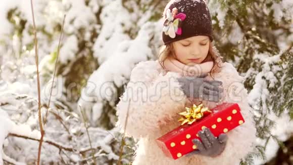 一份圣诞礼物一个穿着粉红色外套的女孩打开一个盒子盒子里有一份礼物背景是一个白雪覆盖的公园令人愉快视频的预览图