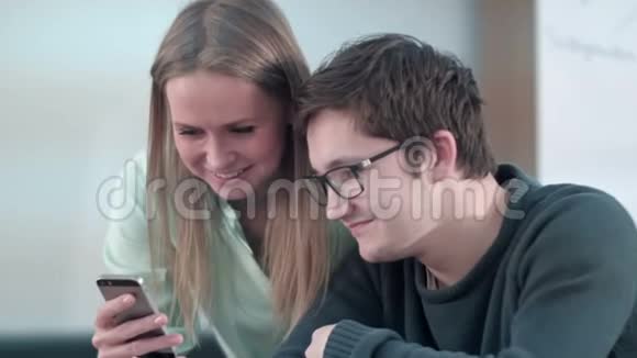 两个年轻的朋友坐在学校的桌子上在智能手机上工作视频的预览图