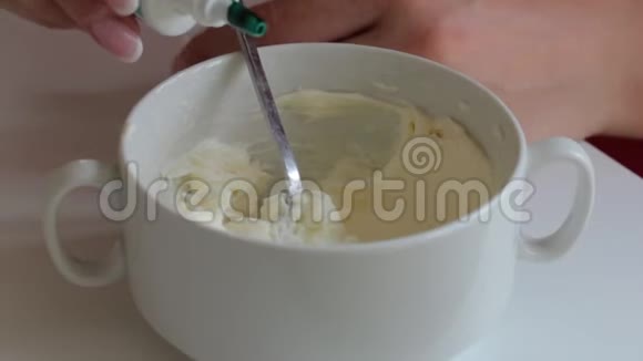 一个女人从一管奶油奶酪中加入一滴食用色素着色奶油以润滑蛋糕视频的预览图