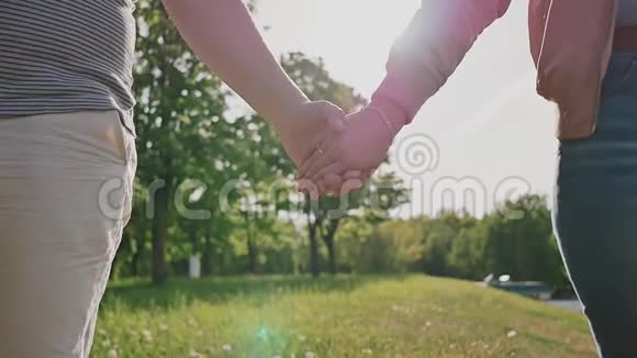 一对浪漫的情侣在绿色的夏天公园里他们在阳光的照射下互相牵着的手特写镜头视频的预览图