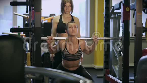 一个肌肉发达的女人穿着弹性西装在一个体育俱乐部里抱着杠铃视频的预览图