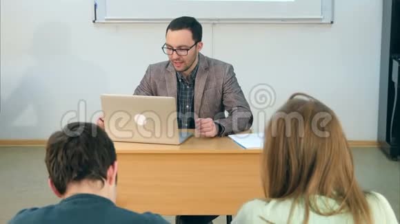 年轻教师坐在教室里手提电脑和学生交谈视频的预览图