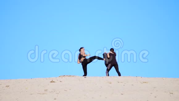 两个穿着黑色健身服的年轻女子在荒无人烟的海滩上做一对踢腿训练比赛视频的预览图